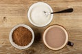 Spoon in bowl with sugar, bowl with cacao powder, cup of cocoa with milk on table. Top view Royalty Free Stock Photo