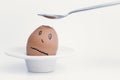 Spoon breaks sad egg on a stand in the form of human head . Royalty Free Stock Photo