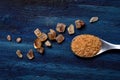 Spoon with brown cane sugar on a rugged blue wooden board, spilled large crystals of brown sugar around