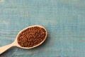 Spoon with buckwheat tea granules on light blue wooden table, top view. Space for text