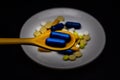 Spoon with capsules, behind it a plate with different colored pharmaceutical pills and capsules.