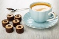 Spoon, chocolate candies, coffee in blue cup on saucer on wooden table Royalty Free Stock Photo