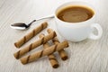 Spoon, coffee with milk in cup, brown wafer rolls with chocolate filling on wooden table Royalty Free Stock Photo