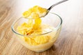 Spoon with with corn flakes and yogurt above bowl on wooden table Royalty Free Stock Photo