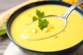 Spoon of delicious creamy corn soup over bowl, closeup