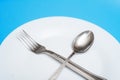 A spoon and a fork lie on an empty plate on a blue background. Diet concept, intermittent fasting