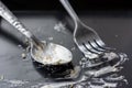 Spoon and fork stained with white cream from cake on dark background.