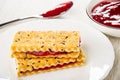 Spoon with jam, bowl with cherry jam, sandwiches from crackers with flax seeds in plate on table