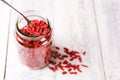 A spoon and jar full of goji berries on white wood