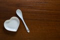 A spoon lies next to a white heart-shaped plate on a wooden table. Ceramic stylish dishes on a nut background. Copy space. Concept Royalty Free Stock Photo