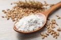 Spoon with organic flour and grains of wheat on wooden table, closeup Royalty Free Stock Photo