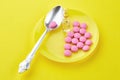 Spoon and pink tablets on saucer, ampoules on yellow background