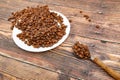 A spoon with roasted coffee lies on a wooden background, next to a white plate with coffee grains Royalty Free Stock Photo