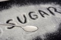 Spoon with sugar, the inscription `sugar` on white sugar. Sugar on a black background. Disease Warning.