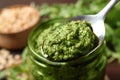 Spoon of tasty arugula pesto near jar with sauce, closeup