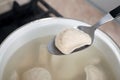 Spoon with tasty dumpling (varenyk) over pot indoors, closeup