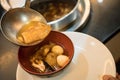 A spoon to scoop Chinese style soup; or braised fish maw in red gravy with eggs, mushroom, and bamboo shoot in white bowl.