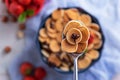 Spoon with trendy cereal pancakes, blue bowl with strawberries on blue gauze, top view