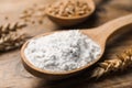 Spoon with wheat flour and spikes on wooden table, closeup Royalty Free Stock Photo