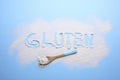 Spoon and word Gluten written with flour on light blue background, flat lay