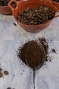 Spoonful of coffee and clay pot of roasted coffee beans on white marble surface