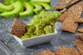 Spoonful of guacamole, set against a bowl and sliced avocado.