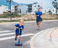 Sport active outdoor family life. Father running blond son riding scooter, mountain summer background, facial