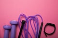 Sport and athletics, dumbbell and skipping rope with a fitness bracelet on a pink background