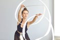 Good looking young female rhythmic gymnast rehearsing element with ribbon in modern gym