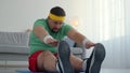 Sport beginner. Chubby man stretching at home, sitting on floor and reaching to his feet, slow motion