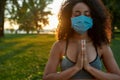 Sport and covid 19. Young mixed race woman wearing protective face mask meditating and practicing yoga outdoors during Royalty Free Stock Photo