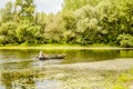 A sport fisherman rides around the pond in a wooden boat