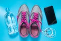 Sport flat lay pink shoes with bottle of water, phone, earphones on blue background. Concept healthy lifestyle and diet Royalty Free Stock Photo