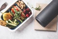 Sport food concept. Lunch box with heathy food, notebook and mat on a gray background