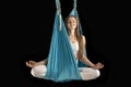 Sport girl practicing fly yoga in hammock and sitting in lotus position in the air. Portrait of woman in hammock on black Royalty Free Stock Photo