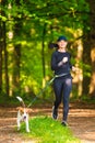 Sport girl is running with a dog Beagle on a leash in the spring time, sunny day in forest