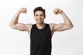 Sport and gym. Smiling young healthy man flexing biceps, showing strong big muscles and fit body, standing in tank top Royalty Free Stock Photo