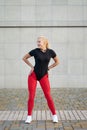 Sport and health. Attractive happy slim girl wearing black shirt, stylish red leggings and white sneakers posing on grey wall Royalty Free Stock Photo