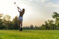 Sport Healthy. Asian sporty woman golf player doing golf swing tee off on the green sunset evening time, she presumably does exerc