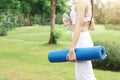 Sport and healthy people in garden concept. Closeup sporty girl holding yoga mat and water bottle walking in park or garden. Royalty Free Stock Photo