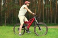 Sport, leisure and healthy lifestyle concept - young man sitting on a bicycle in the forest, male cyclist in profile on grass