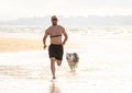 Fitness man running and training with his dog on the beach Royalty Free Stock Photo