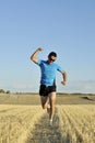 Sport man running outdoors on straw field doing victory sign in frontal perspective Royalty Free Stock Photo