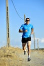 Sport man with sun glasses running on countryside track with power line poles