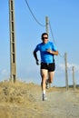 Sport man with sun glasses running on countryside track with power line poles
