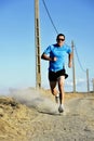 Sport man with sun glasses running on countryside track with power line poles