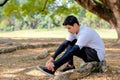 Sport man with white shirt and black legging tie shoelace under branch of big tree during exercise in the garden with copy space