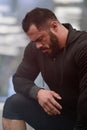 Sport motivation concept of young bearded strong man athlete in sportswear hoodie leaning on knee during pause in