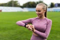 Sport and technology. Young whiteskinned woman with ponytail at running stadium in front of workout uses a sporty smart clock on