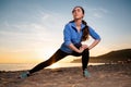 Sport and wellness. A young woman in sportswear stretches her legs. In the background, sunset, sandy beach and ocean Royalty Free Stock Photo